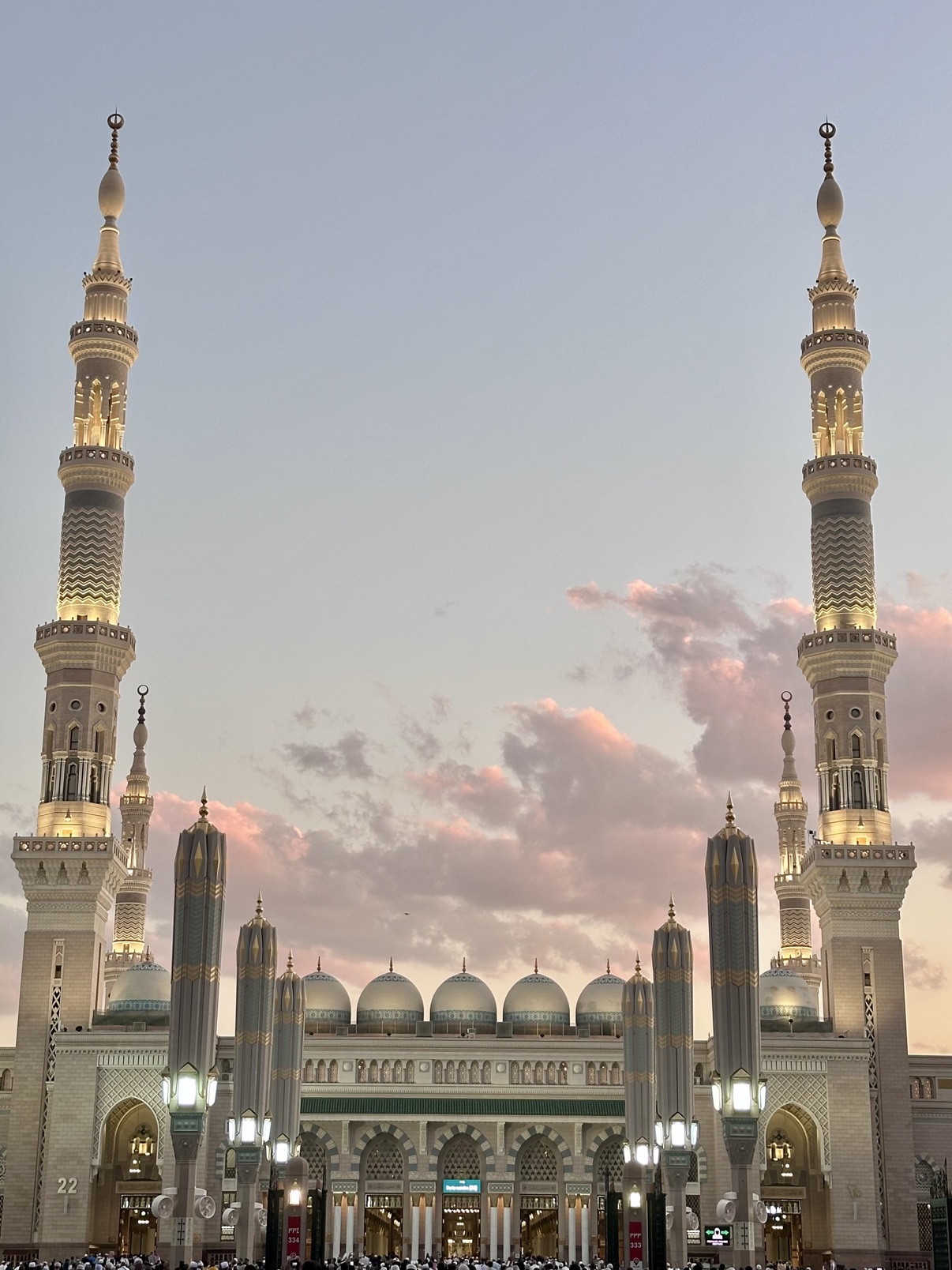 The minarets and umbrellas of the Prophet's Mosque in Madinah against a pink sunset sky