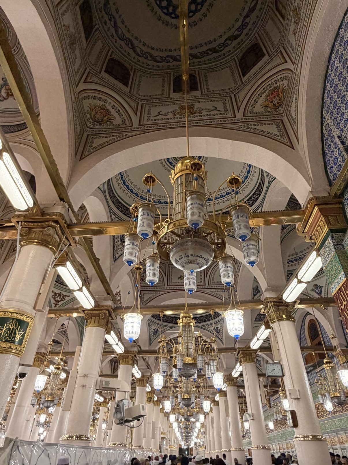 A domed ceiling and ring of chandeliers inside the Prophet's Mosque