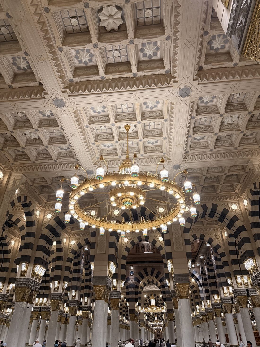 A great golden chandelier and striped arches inside the Prophet's Mosque in Madinah