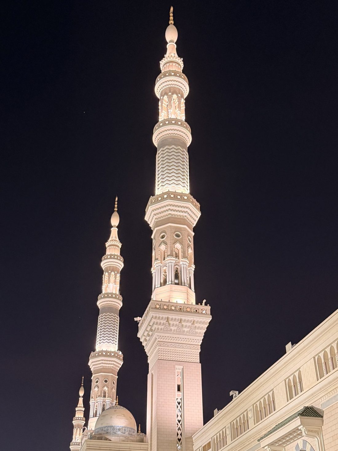The illuminated minarets of the Prophet's Mosque against the night sky