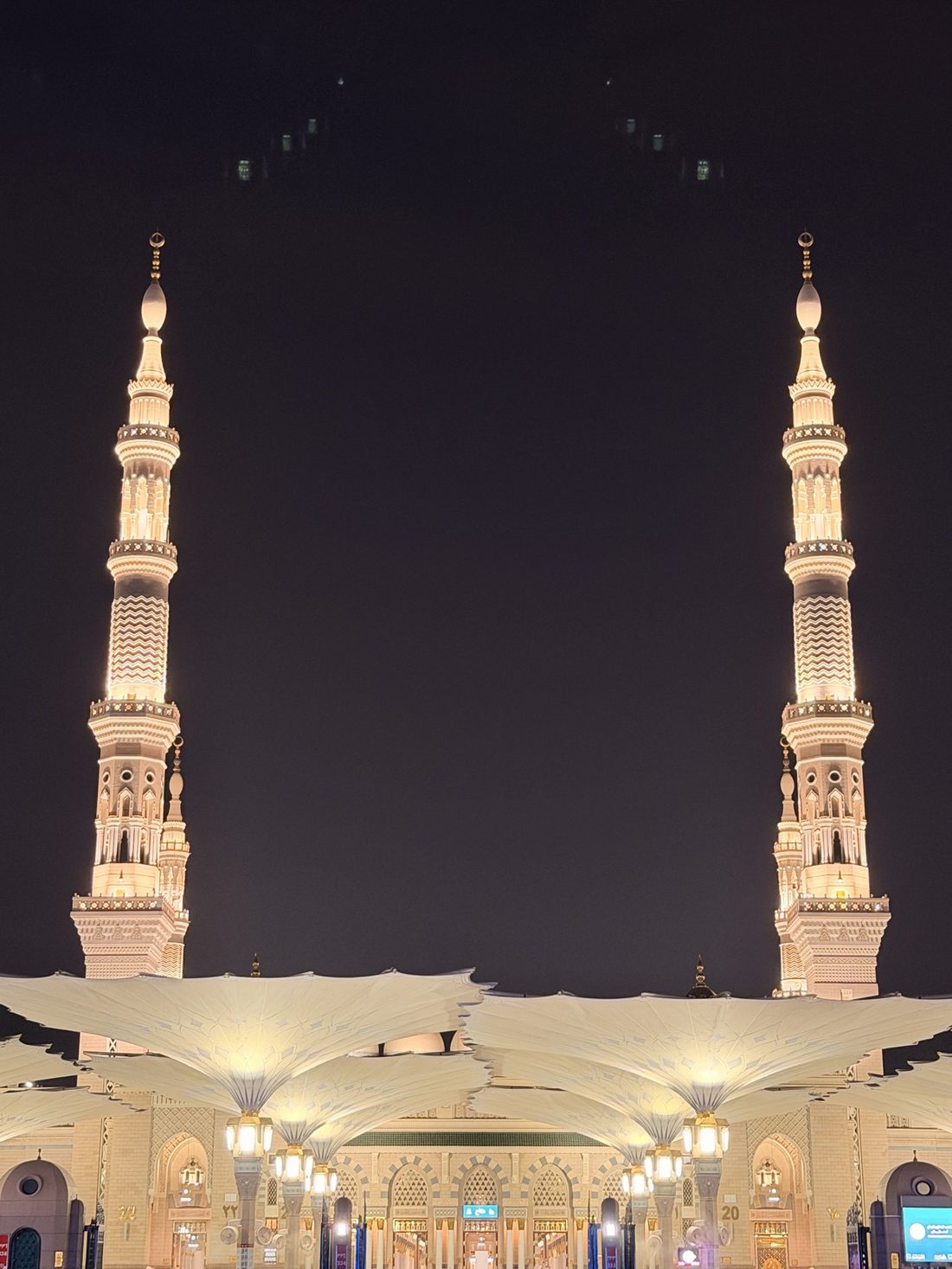 Two illuminated minarets above the courtyard umbrellas of the Prophet's Mosque at night