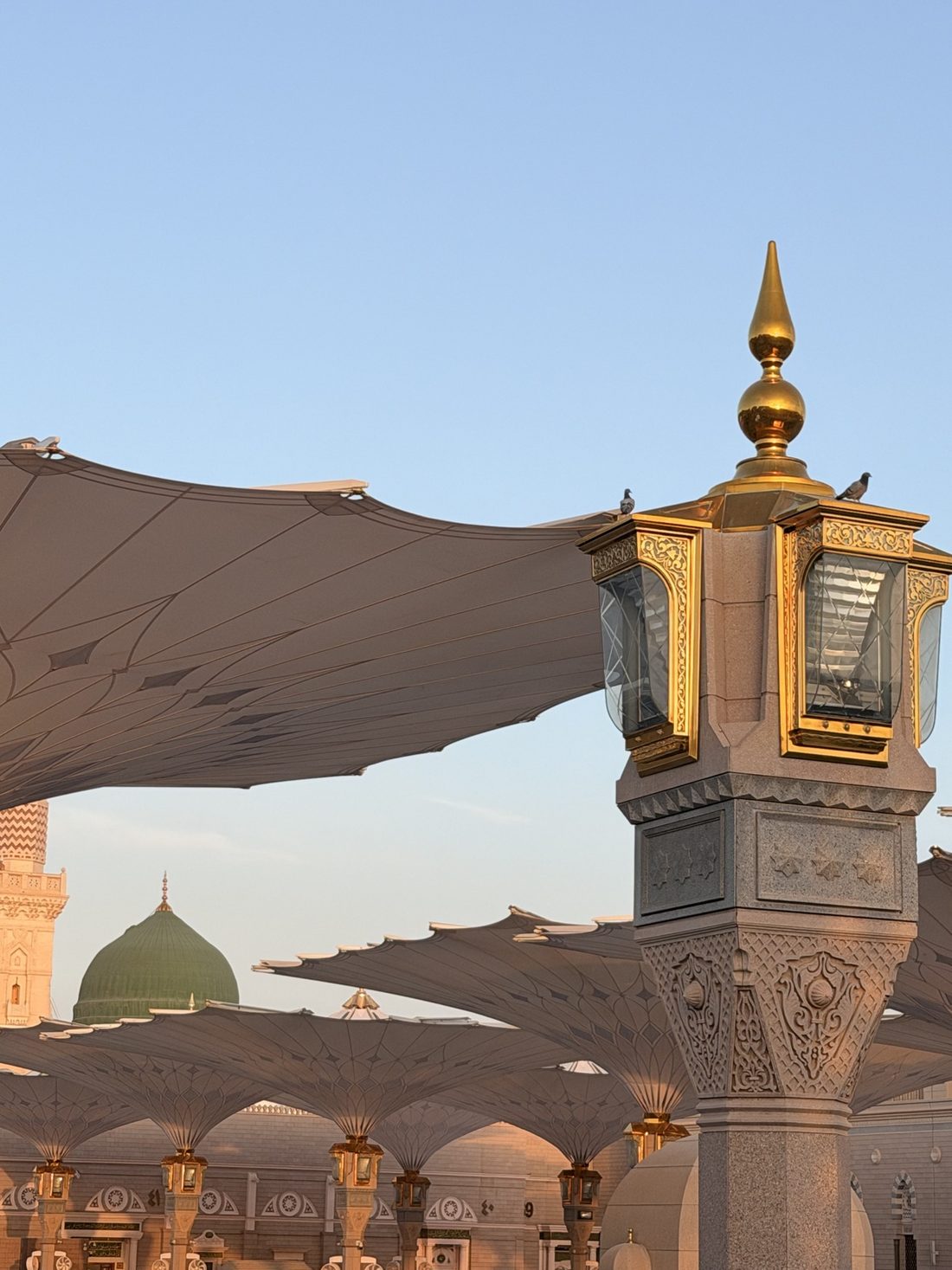 A golden courtyard lamp of the Prophet's Mosque with the Green Dome in the distance
