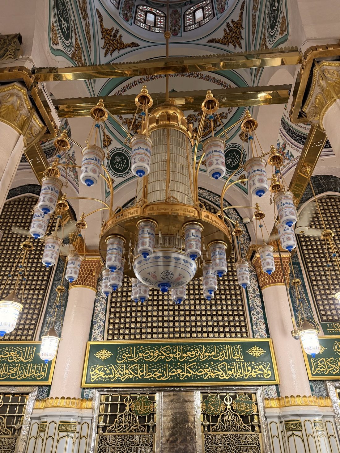 The golden grille of the Sacred Chamber in the Prophet's Mosque beneath a great chandelier