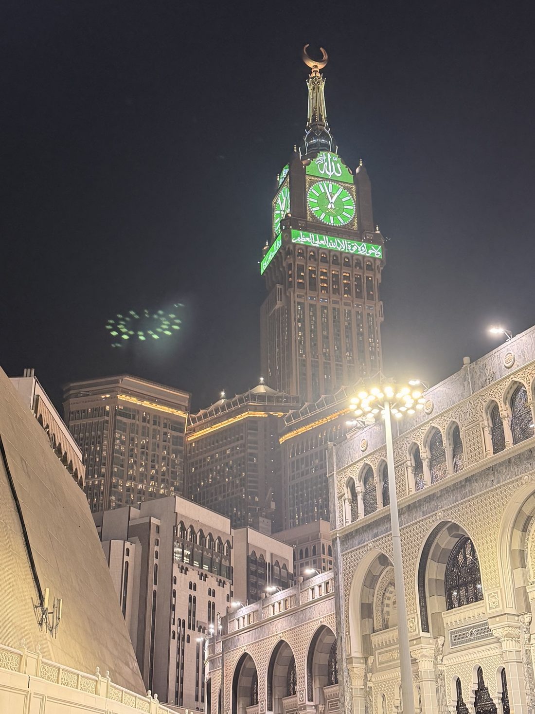 The Makkah clock tower glowing green above the Grand Mosque at night